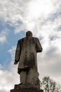 Statue of back of man, one arm folded against blue cloudy sky.