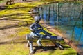 A statue of a boy sitting on a log fishing on the banks of the lake surrounded by lush green moss and still green lake water