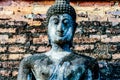 A statue of a Buddha with a stone face stands in front of a brick wall Royalty Free Stock Photo