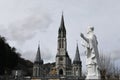 Statue of a catholic saint with praising hands against the backdrop of the lourdes sanctuary in winter