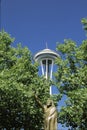 This is a statue of Chief Seattle in front of the Space Needle. There is green summer foliage on the trees surrounding the