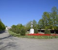 Statue of a collective farmer on a pedestal. The legacy of the Soviet era. A flower bed with tulips and young trees in