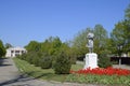 Statue of a collective farmer on a pedestal. The legacy of the Soviet era. A flower bed with tulips and young trees in