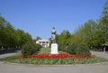 Statue of a collective farmer on a pedestal. The legacy of the Soviet era. A flower bed with tulips and young trees in