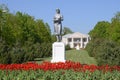 Statue of a collective farmer on a pedestal. The legacy of the Soviet era. A flower bed with tulips and young trees in