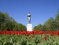 Statue of a collective farmer on a pedestal. The legacy of the Soviet era. A flower bed with tulips and young trees in