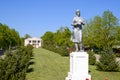 Statue of a collective farmer on a pedestal. The legacy of the Soviet era. A flower bed with tulips and young trees in