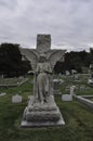 Damaged Angel Statue with One Arm Missing and Spread Wings on a Cross Looking Down in a Cemetery Royalty Free Stock Photo