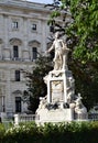 Statue dedicated to Mozart, photographed with a frame of leaves and of a historic building, in the garden and park in the museum d