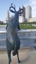 A statue of a deer standing leaning on a bridge rail over looking the city