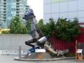 Statue of a dinosaur made out of recycled metal surrounded by trees and buildings