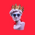 Statue. Earphone on a red background. Gypsum statue of David`s head. Creative. Plaster statue of David`s head in blue sunglasses