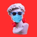 Statue. Earphone on a red background. Gypsum statue of David`s head. Creative. Plaster statue of David`s head in sunglasses and