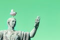 Statue of emperor Caesar Nervae August with gull on the head. Man taking selfie. Humor concept. Green mint background Royalty Free Stock Photo