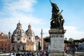A statue in front of Vittoriano with Saint Mary of Loreto Church and Trajan Column in background in Rome, Italy