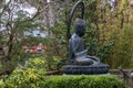 a statue in The Japanese Tea Garden with lush green trees, plants and grass and an orange pergola at Golden Gate Park Royalty Free Stock Photo