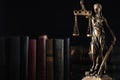 Statue of Lady Justice near books on dark background, space for text. Symbol of fair treatment under law
