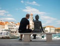 Statue of a little girl pointing at the belltower in a small village of Sutivan in Croatia. Man sitting next to the girl and