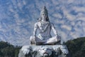 Statue of meditating Hindu god Shiva against the sky and clouds on the Ganges River at Rishikesh village in India