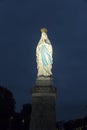 Statue of Our Lady of Immaculate Conception after dark against a dark sky in Lourdes, France