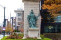 A statue in the park surrounded by autumn colored trees, colorful flowers and lush green plants near the Triumphal arch