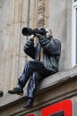 The statue of a photographer sitting on the ledge of the building on a square in Cologne