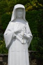 Statue of polish Saint Faustyna Kowalska holding cross and rosary, touching her heart, decorative shrubs in background. Royalty Free Stock Photo