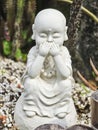 A statue of a small white monk, depicted in a pose of see no evil, hear no evil, speak no evil.