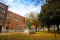 A statue of two men shaking hands surrounded by a red brick building with boarded up windows and autumn colored trees