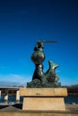 Statue of the Warsaw Mermaid on the banks of the river with a bridge in the background