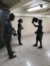 Statues of commuters buying tickets in front of newspaper boy