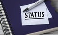 STATUS - word in a white notebook against the background of a black notebook with a pen