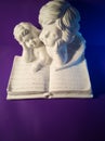 Two white angels and a book on a purple background figurine Royalty Free Stock Photo