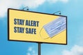 Stay Alert Stay Safe warning sign with smiling face mask on blue sky background. Large billboard with the message text