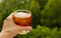 Stay at home balcony cocktail party. Classic home-made Old Fashioned alcohol drink with ice ball and orange zest, trees sky and