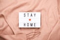 Stay home concept. STAY HOME written on light board on cozy peach plaid. Self isolation during Covid-19 coronavirus pandemic