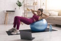 Stay home. Young girl doing exercises with fitness ball while watching online tutorials on laptop