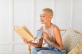 Stay home hobbies concept. Young lady reading book with cup of hot beverage, sitting in wicker chair in living room