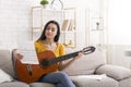 Stay home hobbies. Young girl with music sheet playing guitar on sofa in light room, copy space