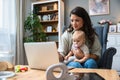 Stay at home mom working remotely on laptop while taking care of her baby. Young business mother on maternity leave trying to Royalty Free Stock Photo