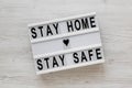 `Stay home stay safe` words on a lightbox on a white wooden background, top view. Overhead, from above, flat lay