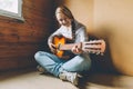 Stay Home Stay Safe. Young woman sitting in room on floor and playing guitar at home. Teen girl learning to play song and writing Royalty Free Stock Photo