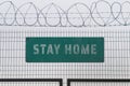 Stay Home sign on barbed wire fence, a digital composite. Tough lockdown measures restrict rights of people