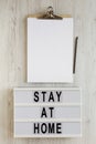 `Stay at home` words on a modern board, clipboard with blank sheet of paper on a white wooden background, top view. Overhead, fr Royalty Free Stock Photo