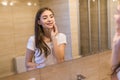 Staying fresh and clean. Beautiful young woman touching her face with sponge and smiling while standing in front of the mirror