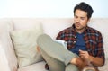 Staying in the know. a handsome young man reading a newspaper on the sofa at home. Royalty Free Stock Photo