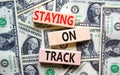 Staying on track symbol. Concept words Staying on track on wooden blocks on a beautiful background from dollar bills. Business,