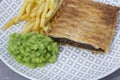 Steak and onion lattice pie with fries and mushy peas. Royalty Free Stock Photo