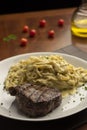 Steak with pasta tagliatelle fetuccini on plate with blurred background with tomatoes olive oil and wine glass