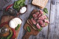 Steak sandwich, sliced roast beef, cheese,spinach leaves,tomato. Rustic,on a wooden surface